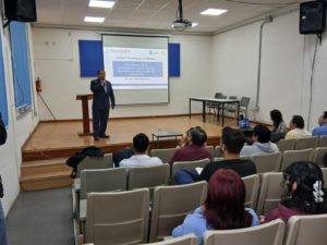 El Dr. Giner Alor Hernández de pie en el escenario, impartiendo la ponencia “Importancia de la Investigación y Publicación Científica en Estudiantes de Doctorado” con una diapositiva proyectada detrás de él.