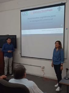 La Dra. María del Carmen Mezura Godoy dirigiéndose a los asistentes desde el escenario, con la proyección del título del seminario en pantalla.