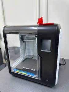 Esta es una impresora 3D, utilizada para crear objetos tridimensionales a partir de un diseño digital. Funciona mediante la deposición capa por capa de material (generalmente plástico) hasta formar la pieza completa.